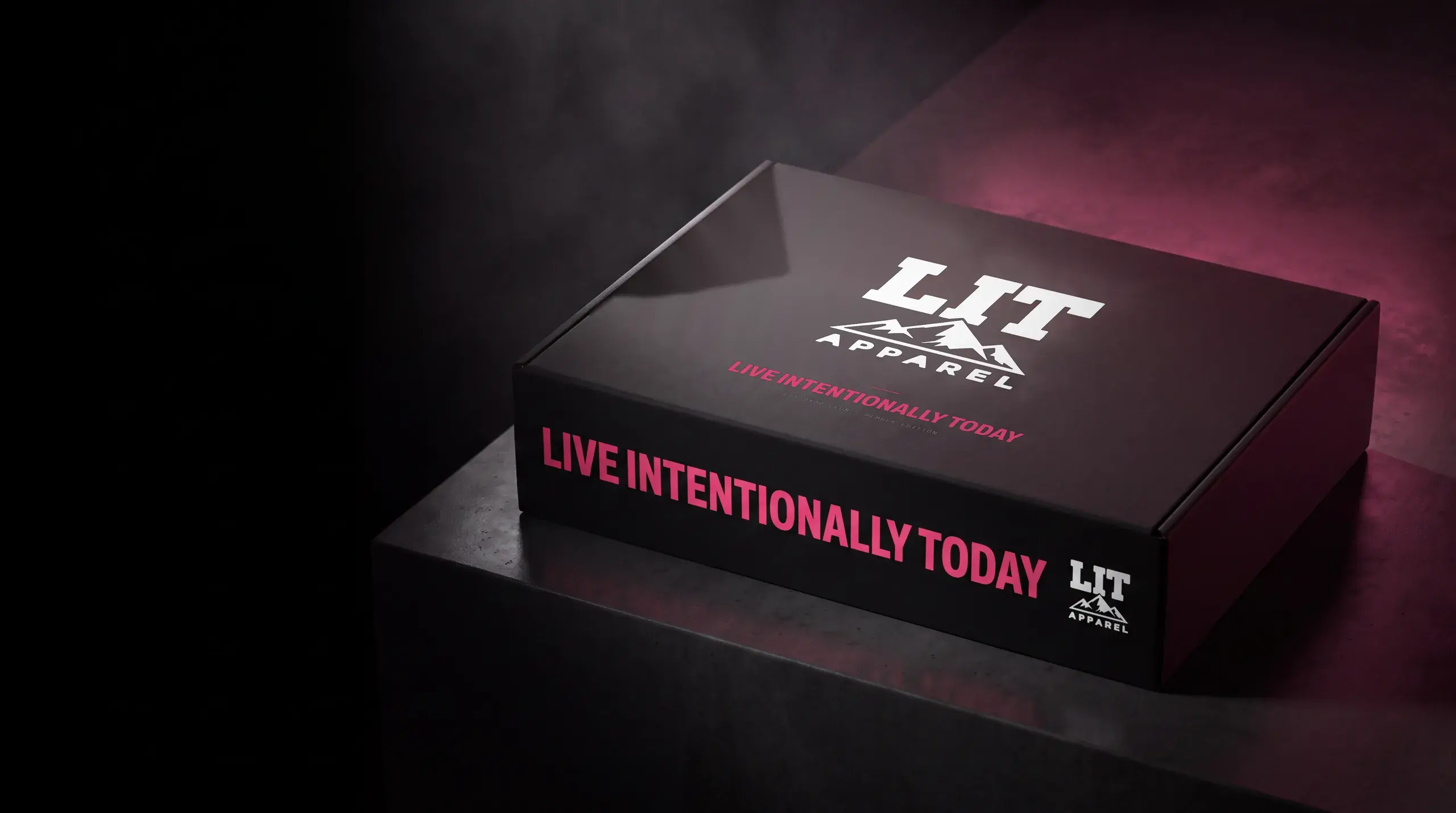 The black LIT Drop Club box, closed, on a concrete plinth: the white LIT Apparel logo on the lid and LIVE INTENTIONALLY TODAY in pink along its side.