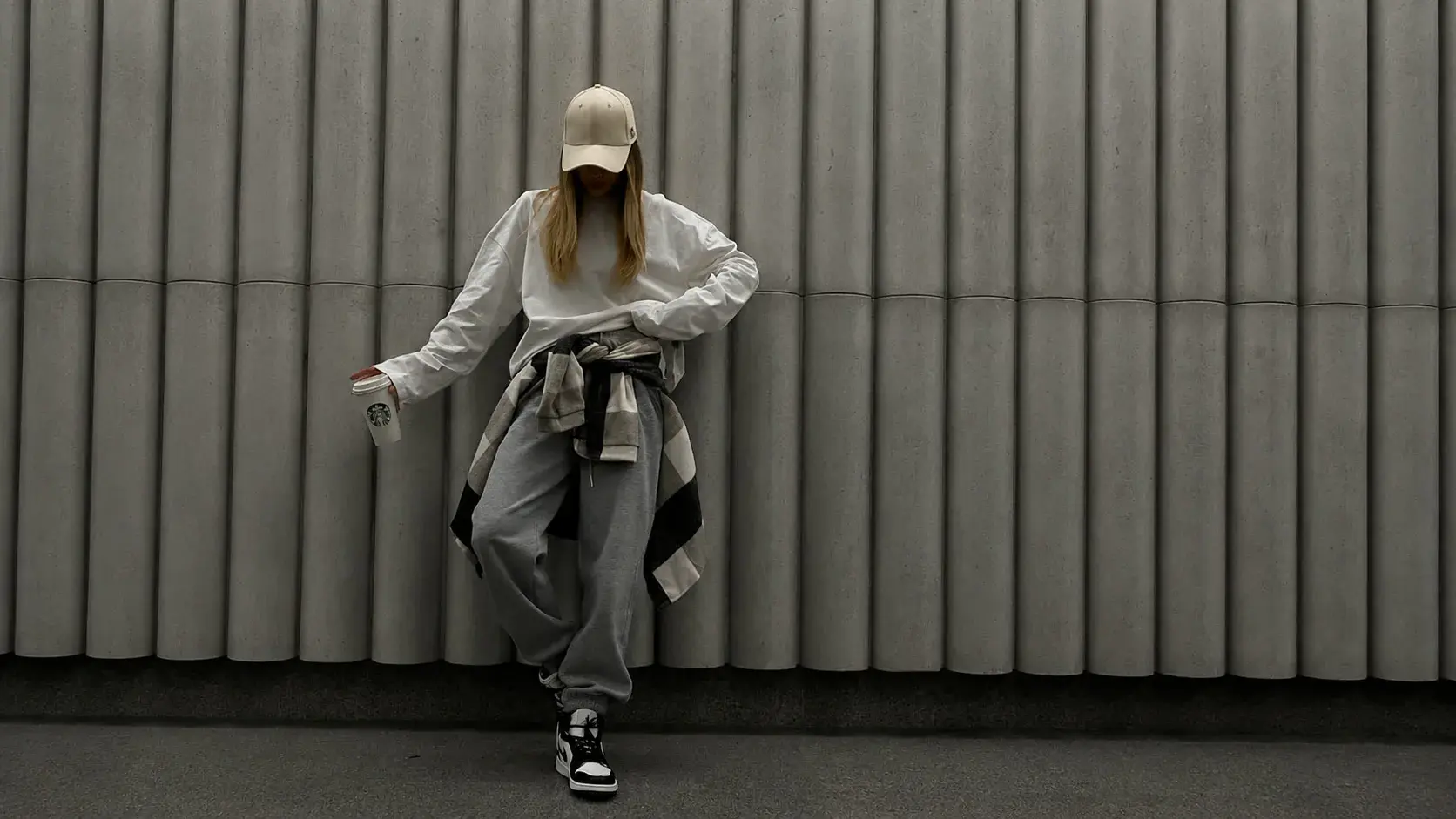 A woman in a grey hoodie and cargo trousers walks past a concrete wall.