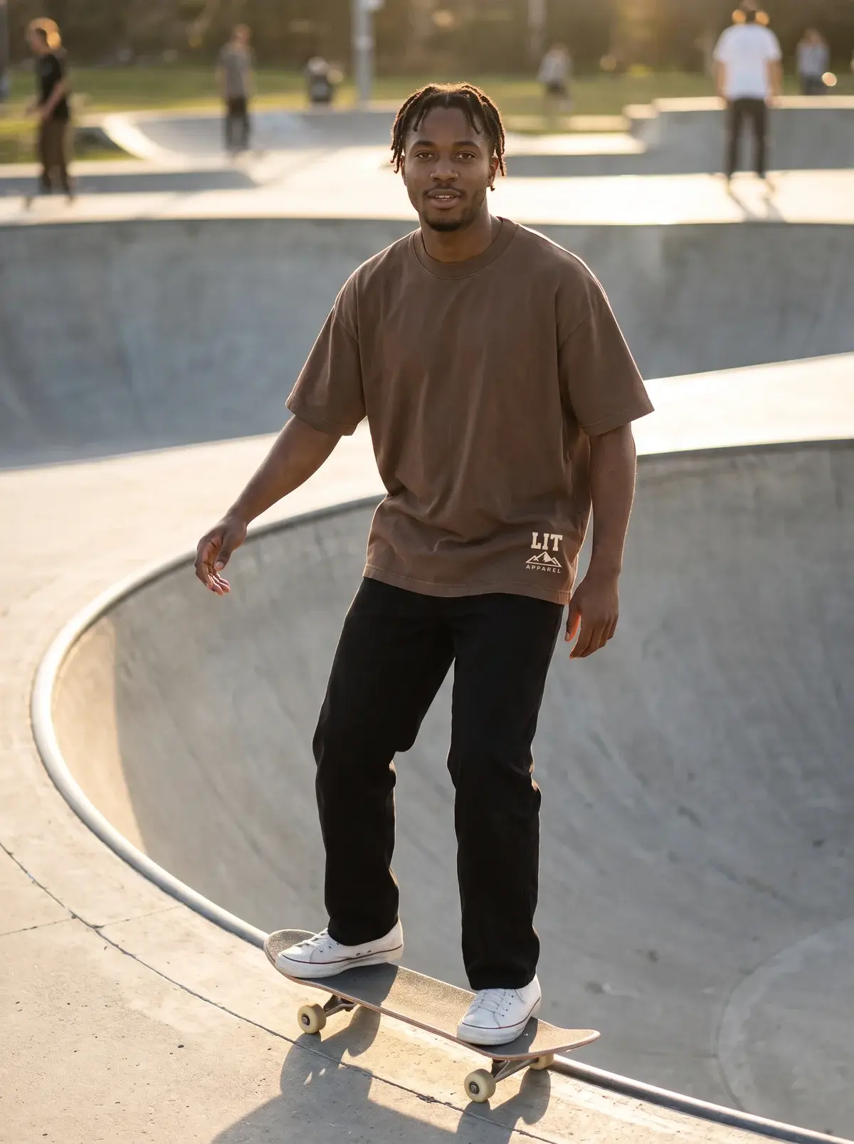 A man skateboarding along the lip of a concrete bowl at golden hour in the cocoa Live Intentionally Tee and black trousers.